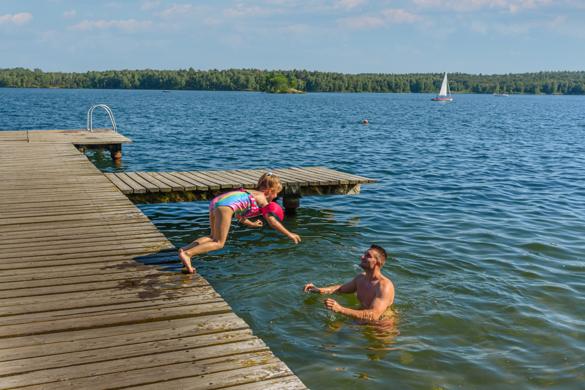 Mädchen spring von einem Steg zu Papa in den See
