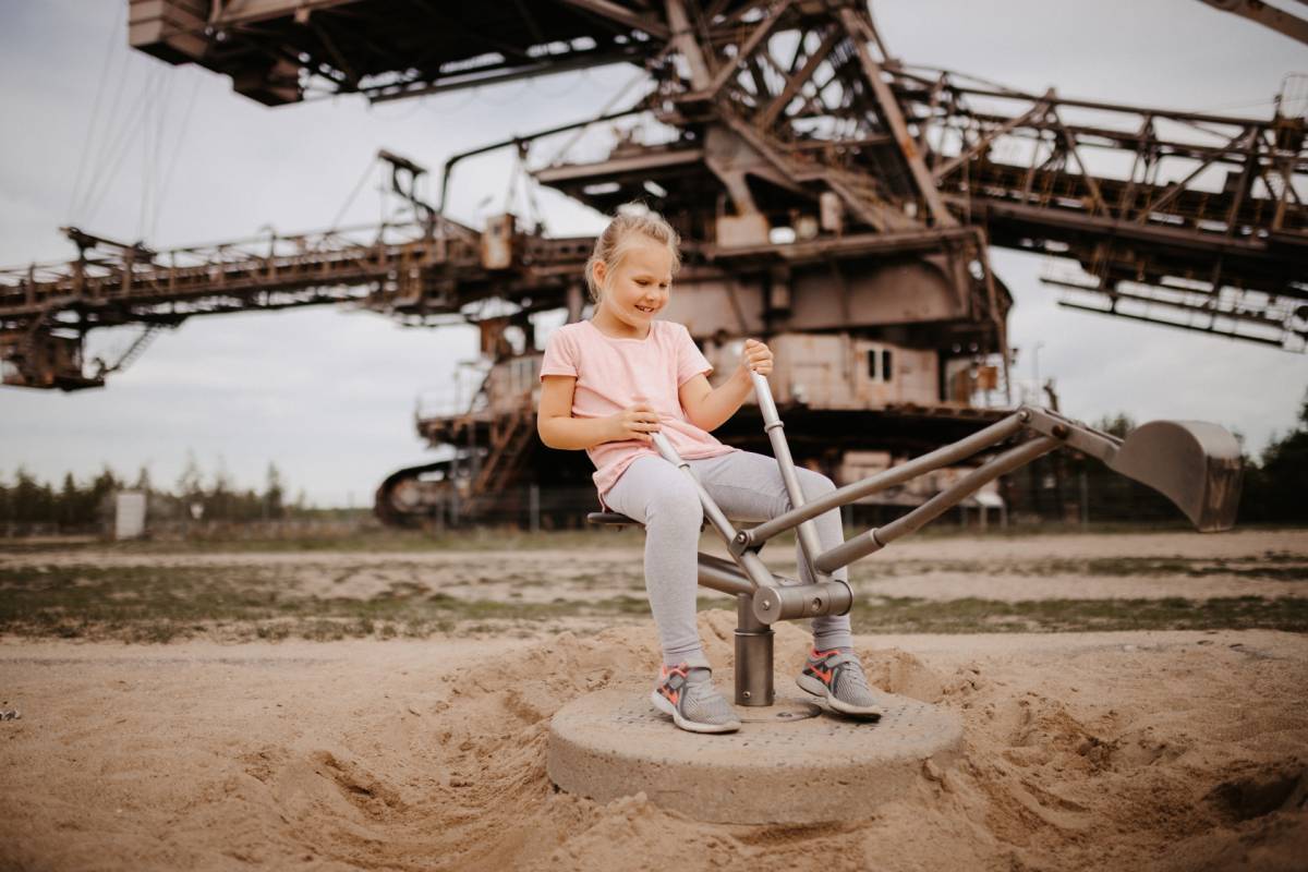ein Mädchen spielt auf einem kleinen Bagger im Sand auf dem Spielplatz auf Ferropolis