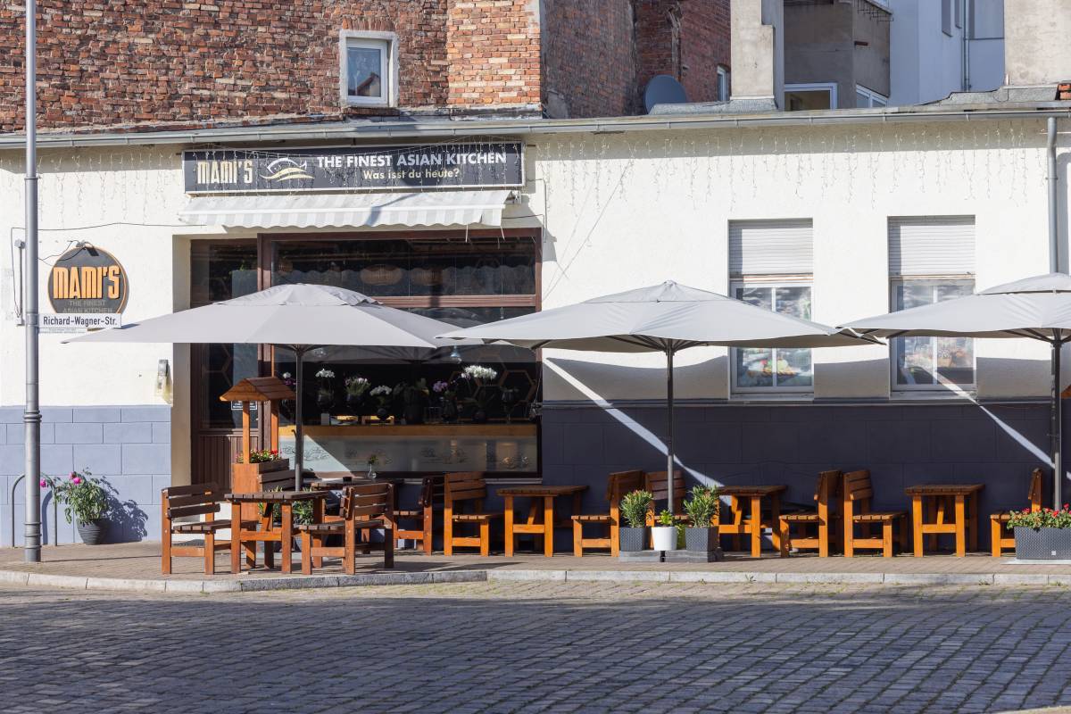 Beschirmter Außensitz- und Essbereich des Mamis Sushi Restaurant Dessau mit Holzbänken und dekorativen Pflanzen.