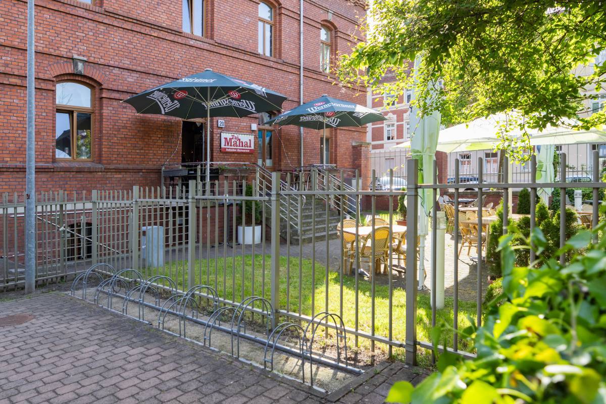 Begr&uuml;nter Au&szlig;ensitz- und Essbereich des Taj Mahal Restaurant Dessau mit beschirmung und auff&auml;lliger Ziegelfassade.