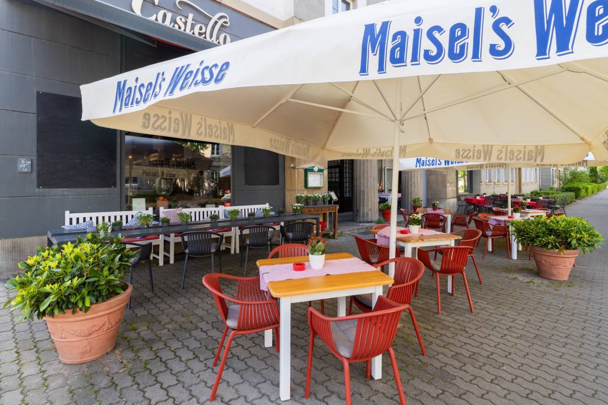 Beschirmter Außensitz- und Essbereich mit roter Markise und geschwungenem Schriftzug auf der dunkelgrauen Fassade des Castello Restaurant Dessau.