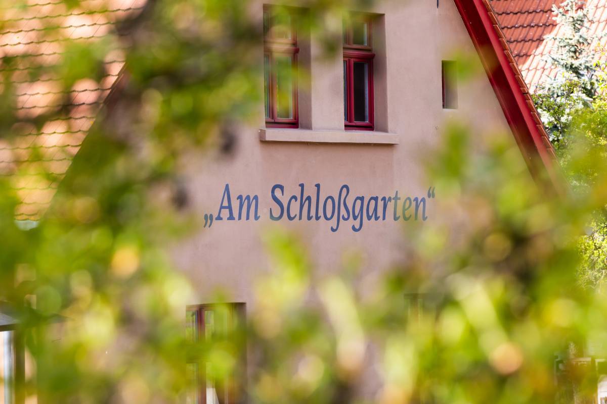 Detailaufnahme des Logos vom Restaurant Am Schloßgarten Dessau in blauer Schrift mit Begrünung im Vordergrund