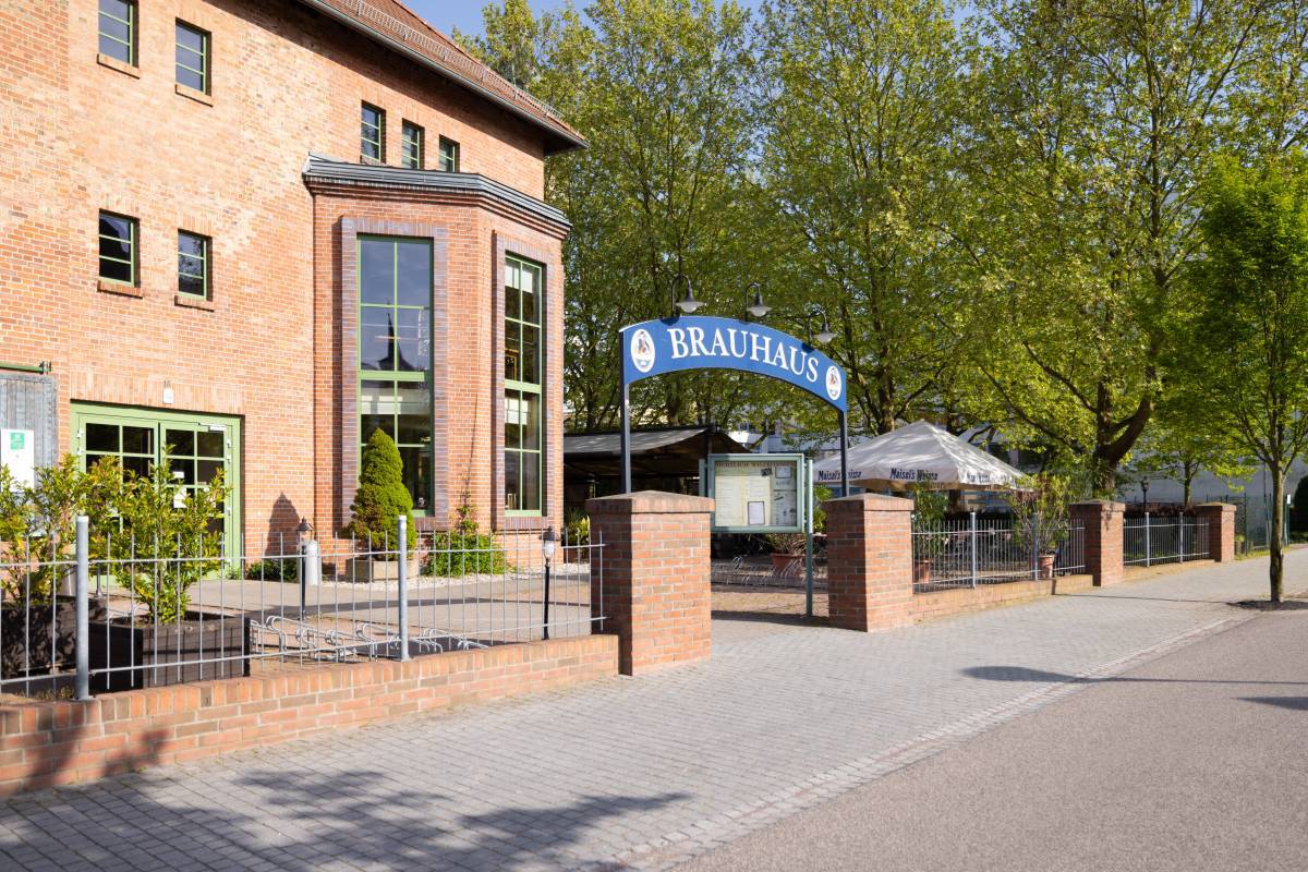 Begrünter Eingangsbereich des Brauhaus "Zum Alten Dessauer" mit blauem Restaurant Schild vor der geziegelten Fassade.