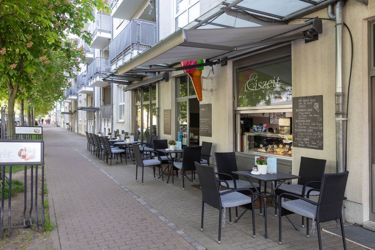 Außensitz- und Eingangsbereich des Eiszeit Eiscafé Dessau mit Begrünung am linken Rand sowei einer Angebotstafel.