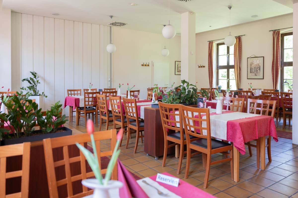Innensitz- und Essbereich des Restaurant am Georgengarten im klassischem Stil mit rot weißem Tischgedeck.