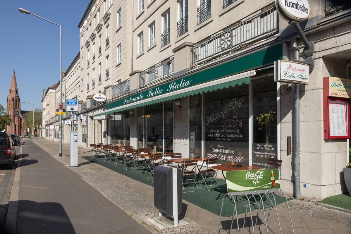 Außensitz- und Essbereich des Restaurant Bella Italia Dessau mit grüner Markise und Kirchturm im Hintergrund.