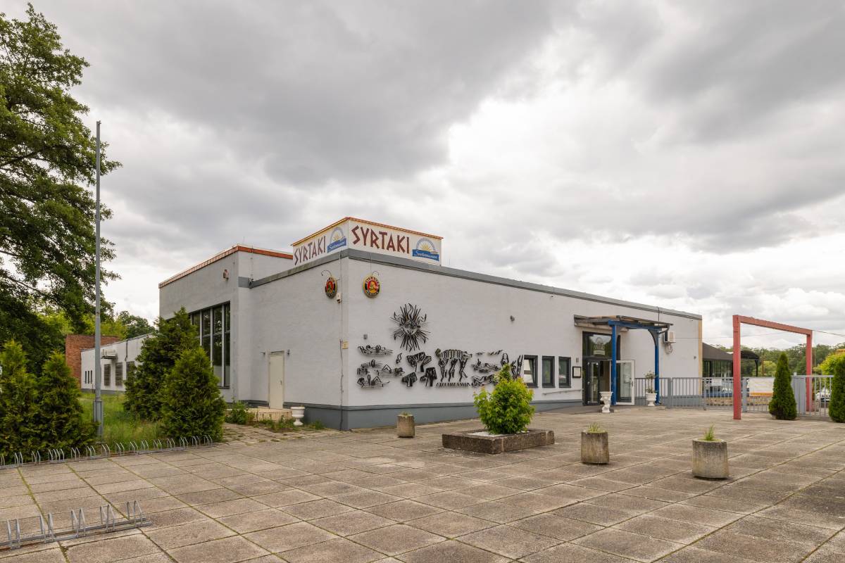 Außenbereich des Syrtaki Restaurant mit Verzierungen an der Fassade und Begrünung
