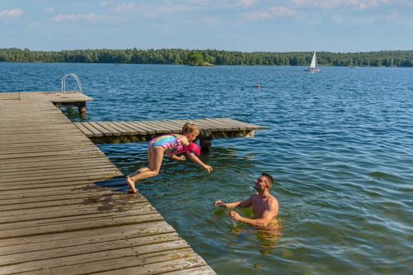 Mädchen spring von einem Steg zu Papa in den See