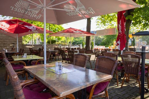 begr&uuml;nter Au&szlig;ensitz- und Essbereich des Restaurant Asado mit roter Beschirmung