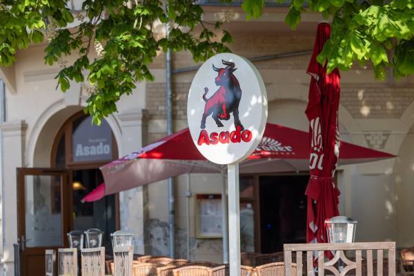 Detailaufnahme vom Restaurantschild Asado in roter Schrift und mit einem Bullenmotiv darauf