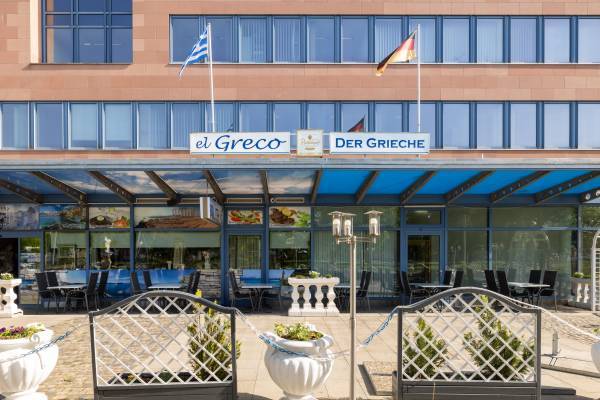 Au&szlig;ensitz- und Essbereich des El Greco Restaurant Dessau mit blauem Fenster Design und Akzenten sowie leichter Begr&uuml;nung im Vordergrund.